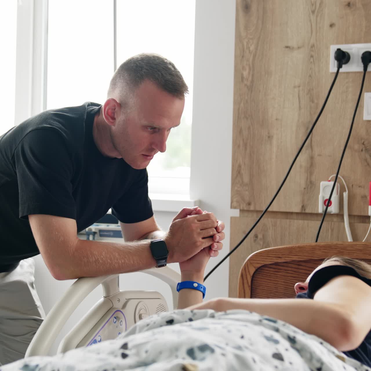 Concerned man holding a hand of his pregnant wife lying in hospital bed. Husband supporting his wife at contractions