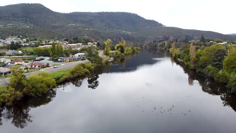 aerial - drone tracking shot of beautiful river winding through a small town in tasmania