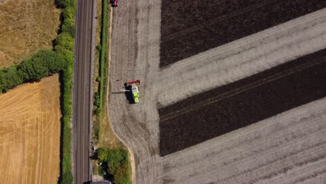 Aerial-shot-of-a-combine-harvester-driving-in-a-field-next-to-train-tracks