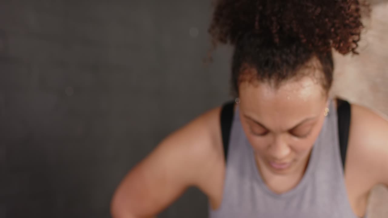 Finishing training, woman in tank top exhaling, tilting head back at gym brick wall for recovery