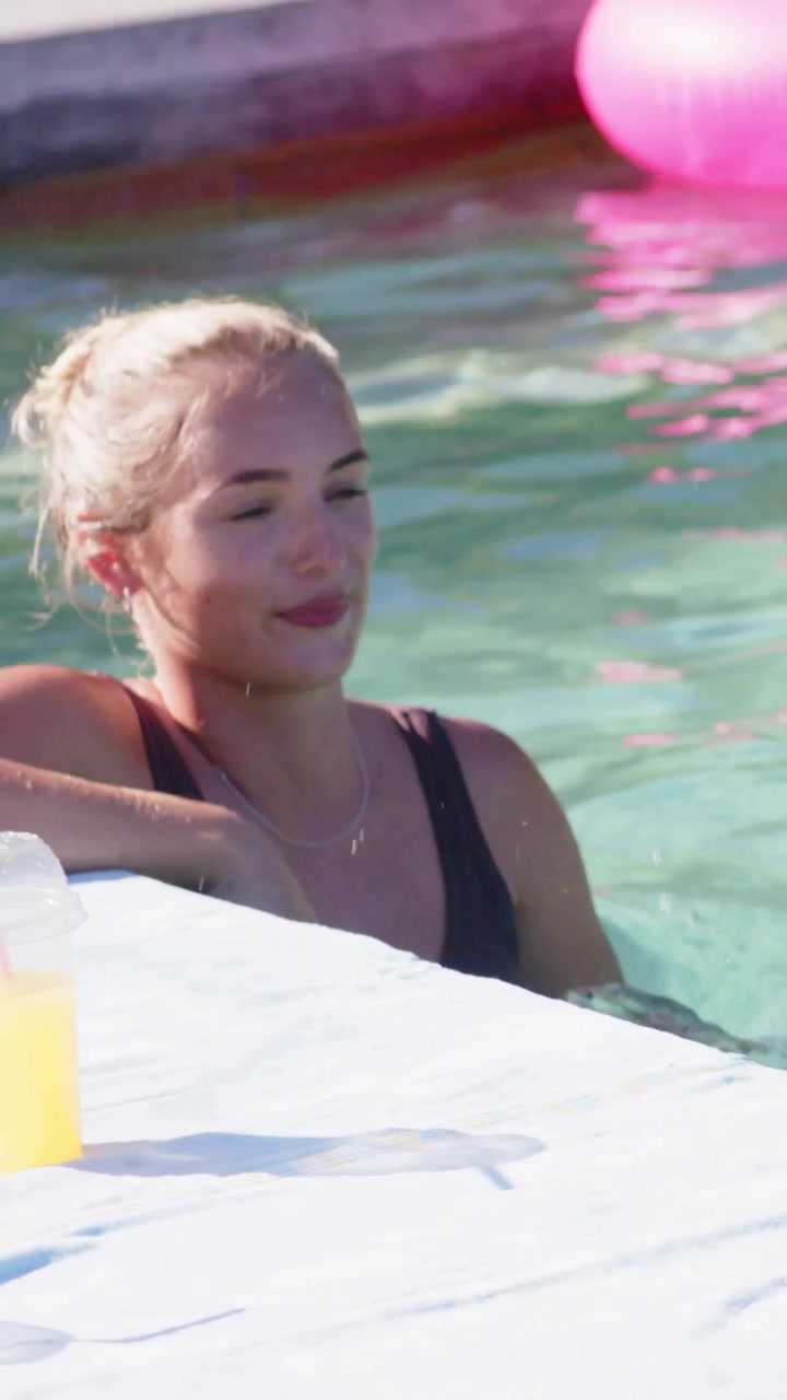 Vertical video: Reaching woman in swimsuit pushing up on pool ledge to rest, showing necklace