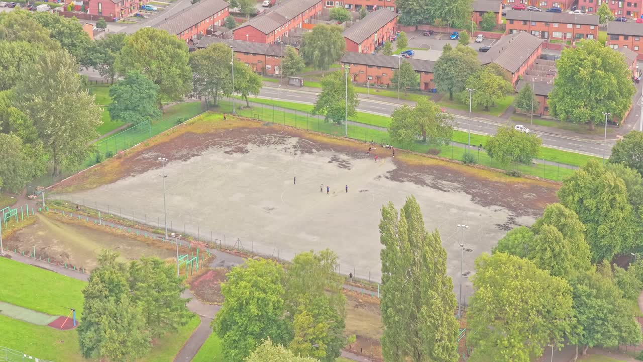 Cleared plot in Salford, likely a former outdoor court now under groundwork amidst housing and green patches—suggesting upcoming redevelopment or sports facility enhancement, static aerial shot