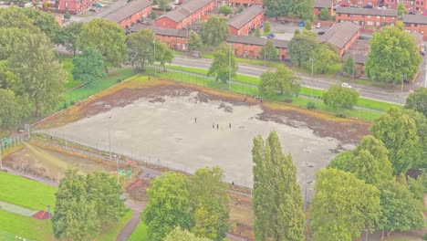 cleared plot in salford, likely a former outdoor court now under groundwork amidst housing and green patches—suggesting upcoming redevelopment or sports facility enhancement, static aerial shot