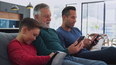 Männliche-Hispanische-Familie-Mit-Mehreren-Generationen-Sitzt-Zu-Hause-Auf-Dem-Sofa-Und-Nutzt-Mobiltelefone-Und-Digitale-Tablets