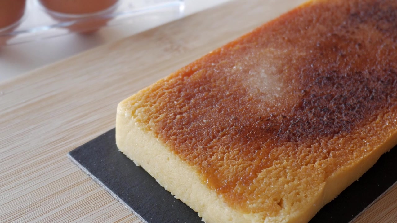 Primer plano de tarta de turrón de yema sobre tabla de madera con huevos, resaltando la textura