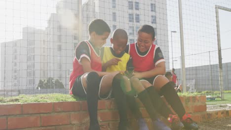 soccer kids in red laughing and using a smartphone in a sunny day