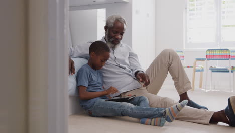 Abuelo-Sentado-Con-Su-Nieto-En-El-Dormitorio-De-Los-Niños-Usando-Una-Tableta-Digital-Juntos