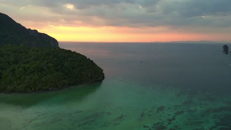 Magischer-Luftbildflug-über-Eine-Tropische-Insel-Bei-Sonnenuntergang-Und-Wolkigem-Himmel-Mit-Booten,-Die-Auf-Einem-Türkisfarbenen-Meer-Segeln