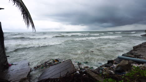 tilt up shot showing crashing waves of ocean reaching polluted beach