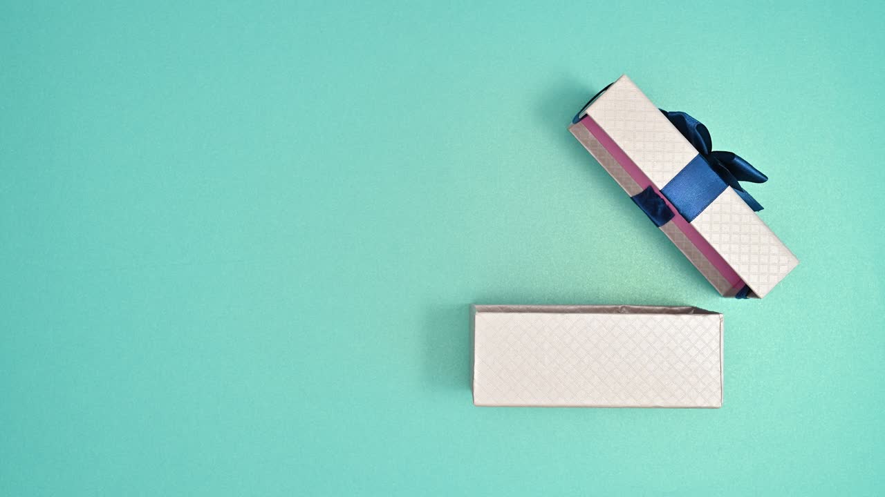 Silver gift with deep blue ribbon appear and open on cyan background. Stop motion