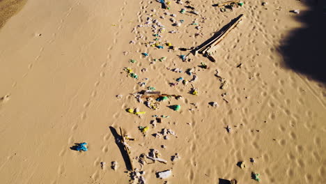 aerial forward view over a beach full with rubbish and footprints