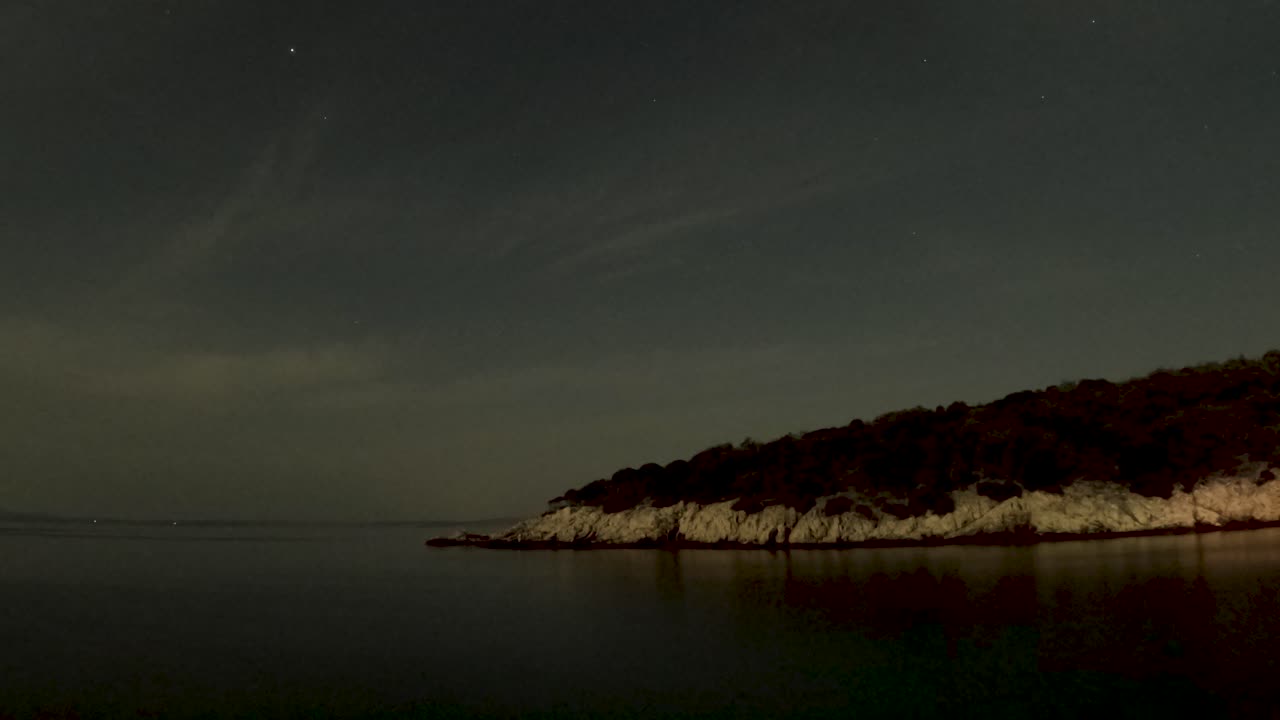 Serene twilight over a calm sea with a dark silhouette of a forested coastline