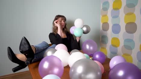 Mujer-Joven-Sentada-En-Una-Mesa-Con-Las-Piernas-Arriba-Reventando-Globos