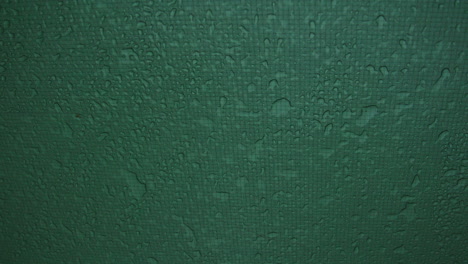 macro detail of green fabric tent wall with raindrops forming textured water pattern across synthetic outdoor tarp