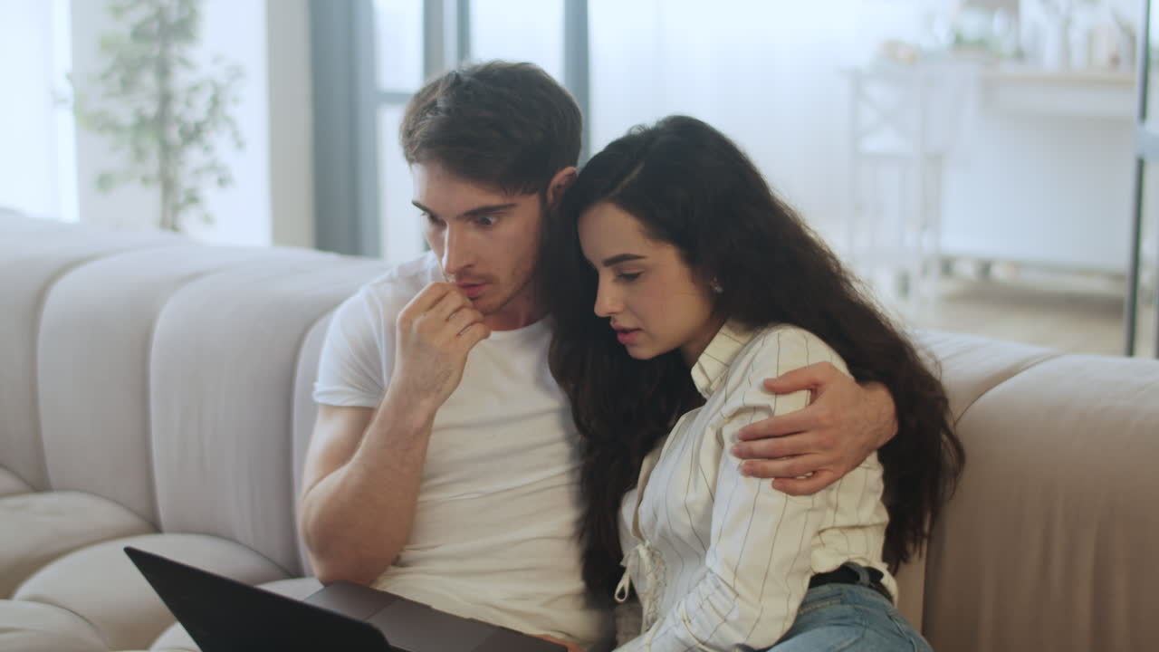 젊은 부부가 슬로우 모션으로 집에서 노트북 컴퓨터를 보고 있습니다.