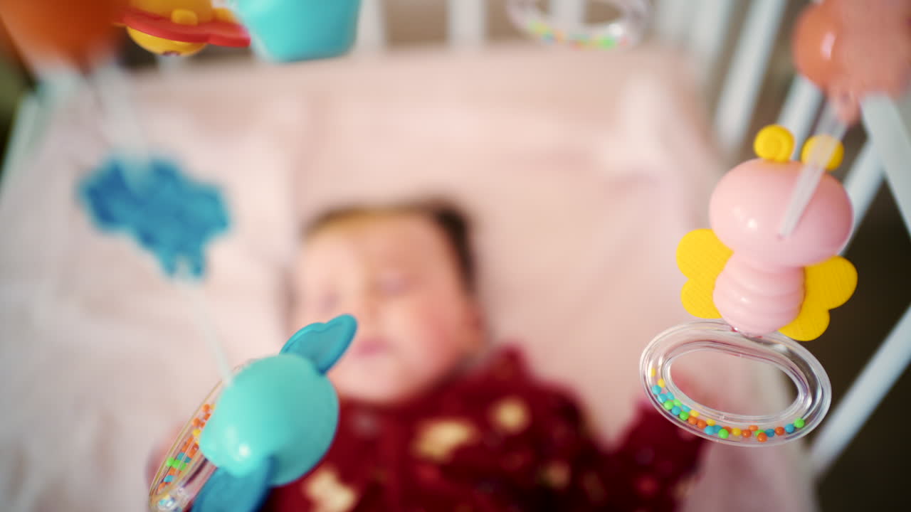 Newborn baby lying in a crib while colorful hanging toys move above
