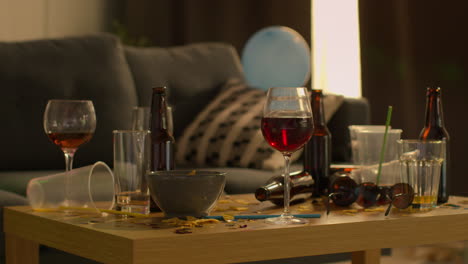 close up of messy lounge or living room with table covered with empty wine glasses and beer bottles after house party 1