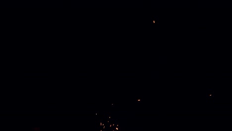 hot red embers from a campfire appear to be sucked from the dark night sky toward the ground