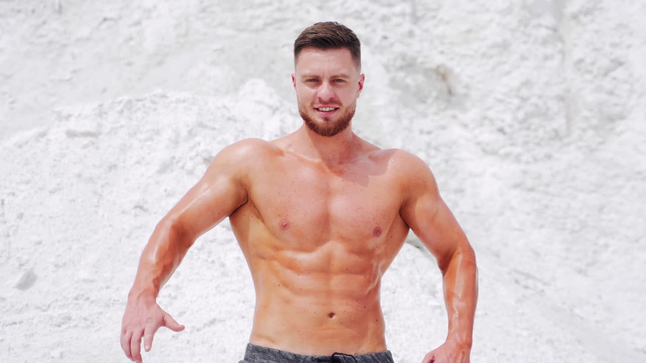 Brutal strong shirtless man shows his large muscles of the body. Bodybuilding in nature on a white mountain background