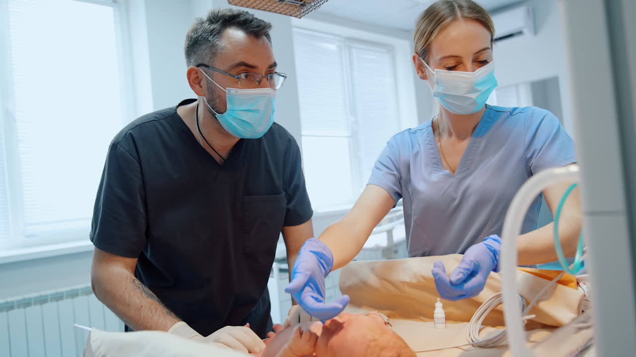 Newborn Caucasian baby lies on the table. Doctors check the child using modern equipment. Neonatologist's examination.