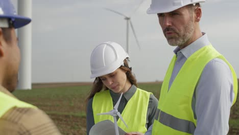 team of caucasian and latin engineers standing on wind turbine field and discussing over project.