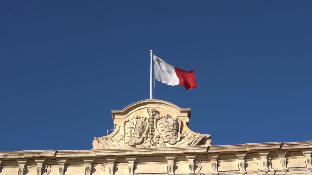 Bandiera di Malta che sventola sopra Piazza della Castiglia a La Valletta con cielo blu sullo sfondo.