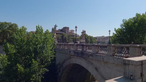 toma panorámica de personas caminando por el puente de san angelo con el río tíber fluyendo por debajo