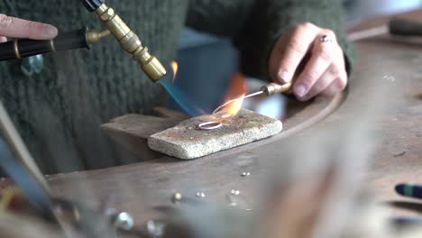 Blow-torch-held-by-female-heating-and-melting-metal-ring-for-creating-an-art-piece,-Close-up-view