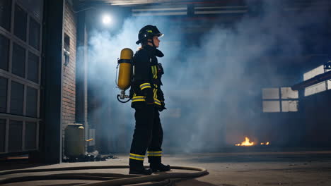 female firefighter standing in smoky building with fire in background