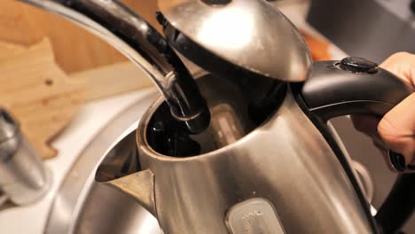 woman filling an electric kettle with water from the kitchen faucet, close-up.