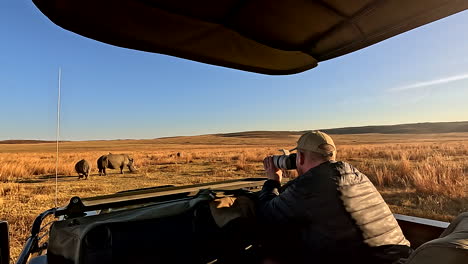 game ranger in safari truck take photos of white rhino in field for research