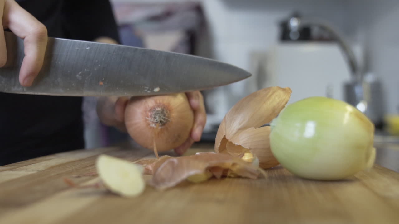 Slow-motion shot as cutting the top and bottom of an onion, to clean to remove onionskin