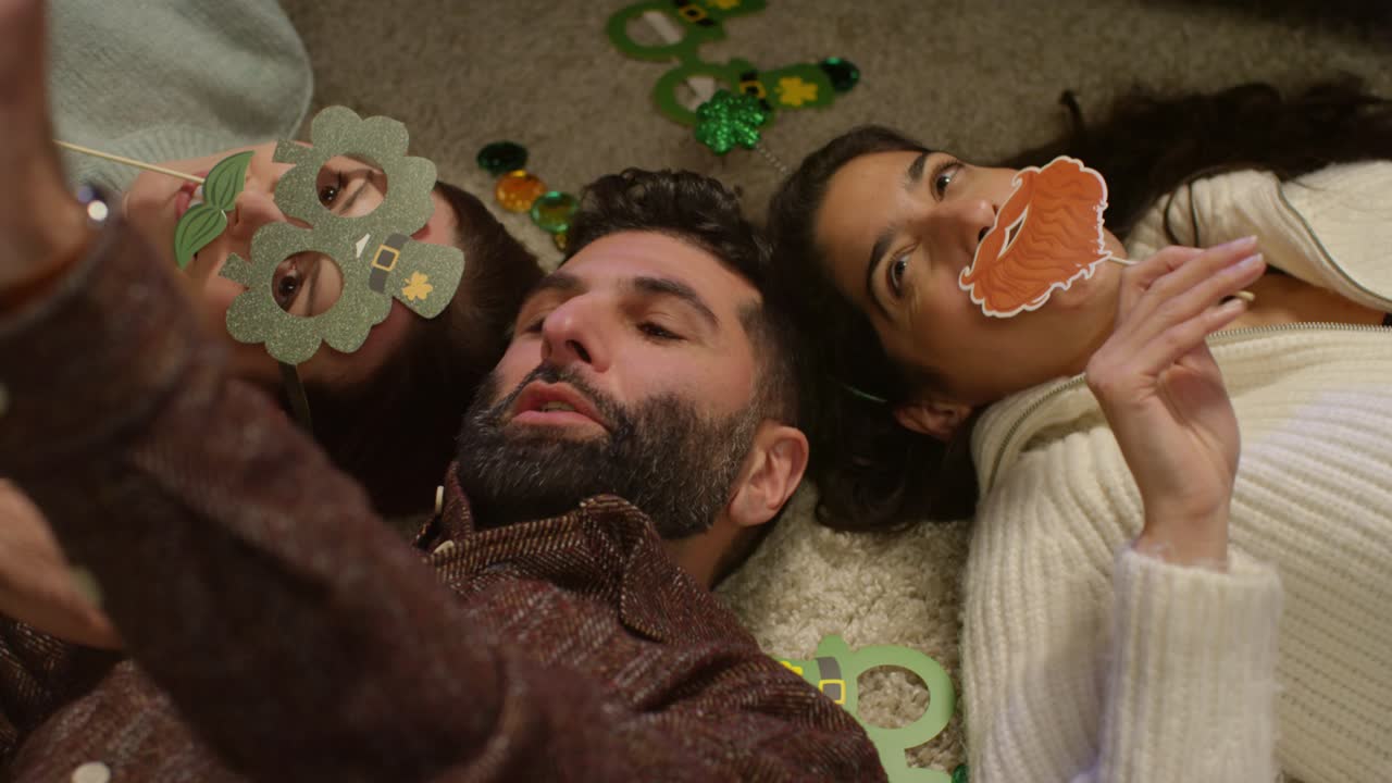 grupo de amigos disfrazándose en casa acostados en el suelo celebrando en la fiesta del día de san patricio posando para una selfie en el teléfono
