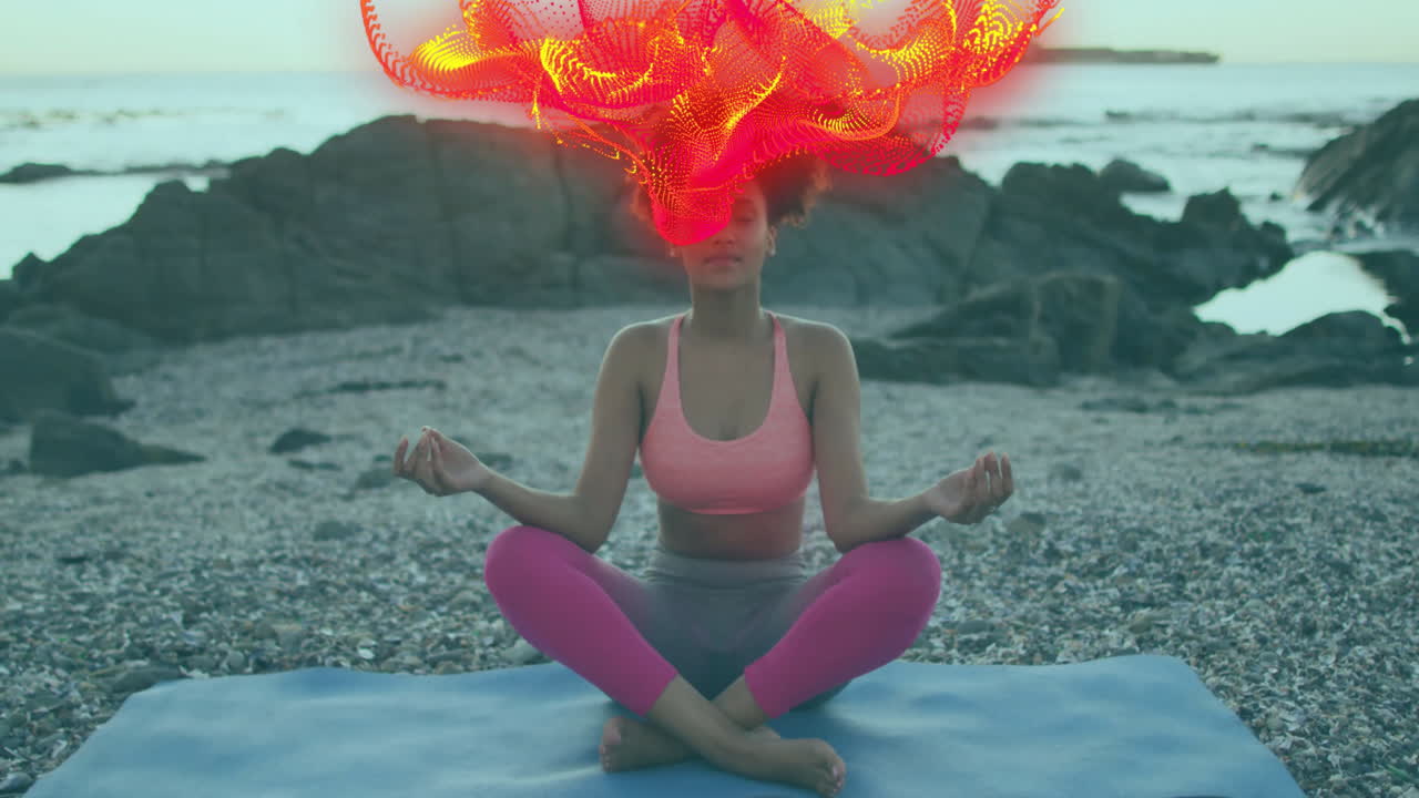 Woman meditating on yoga mat on beach, showing digital brain-activity particles for health