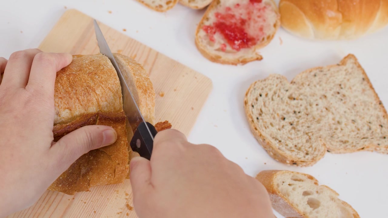 Overhead view of hands cutting sourdough bread with a knife on a white surface.