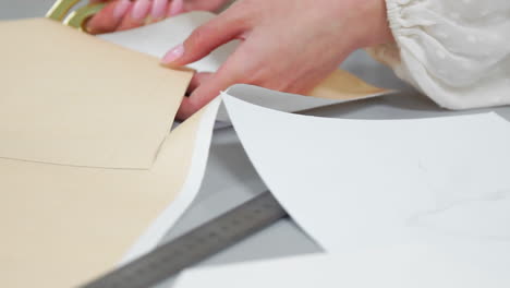 Young-female-designer-with-tape-line-on-her-neck-standing-in-dressmaking-studio-and-drawing-lines-with-chalk-and-rule.-Female-couturier-in-atelier-cutting-out-a-pattern-for-future-clothes.