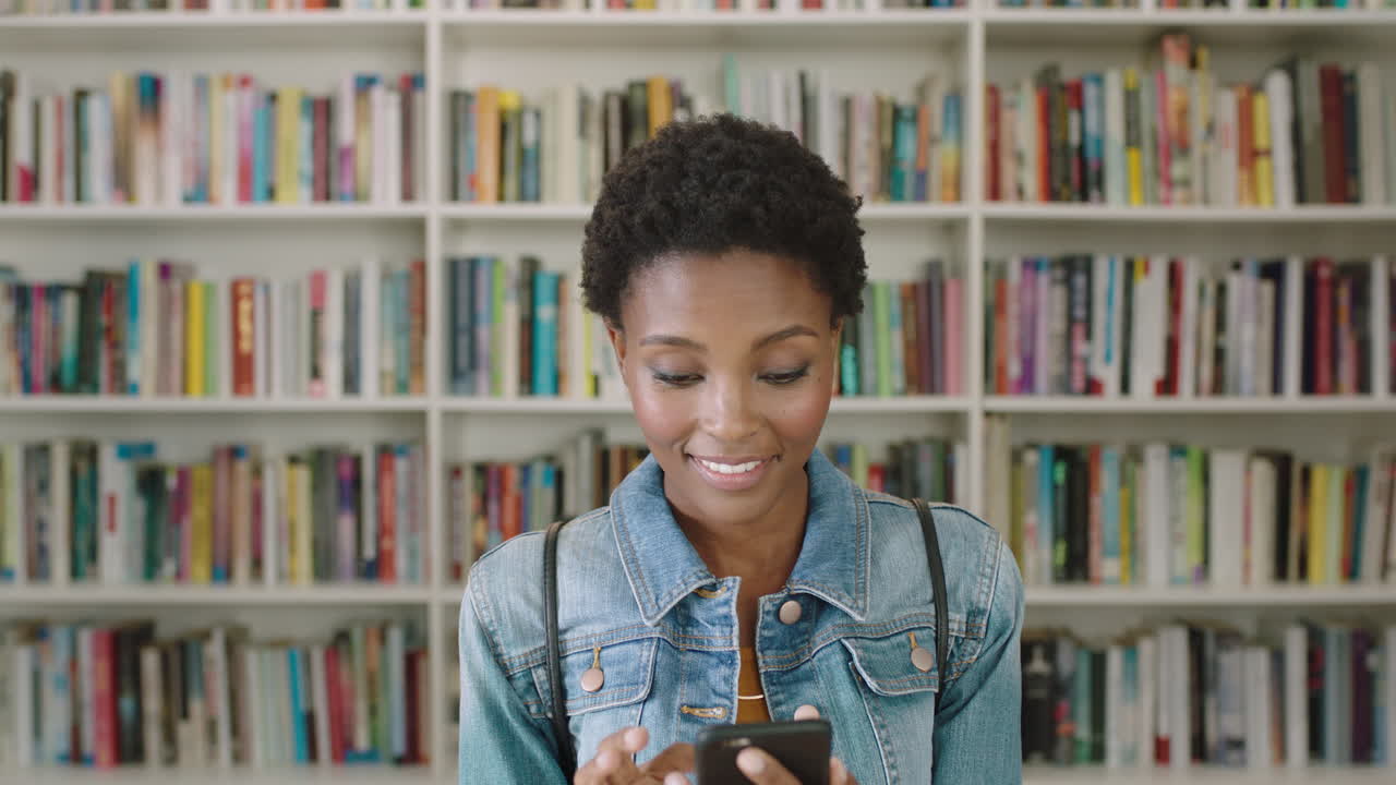 Portrait African American woman student using smart phone bookshelf library university