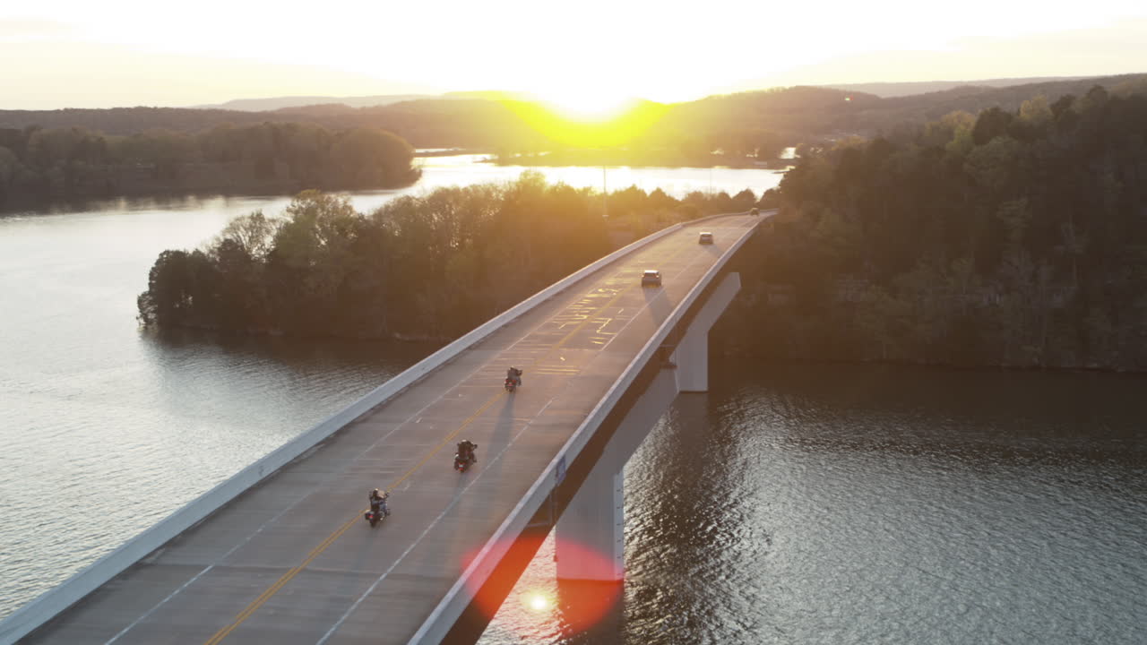 sobrevuelo aéreo siguiendo a un grupo de motociclistas fuera para el fin de semana cruzando un puente en el lago nickajack durante la puesta de sol en tennessee
