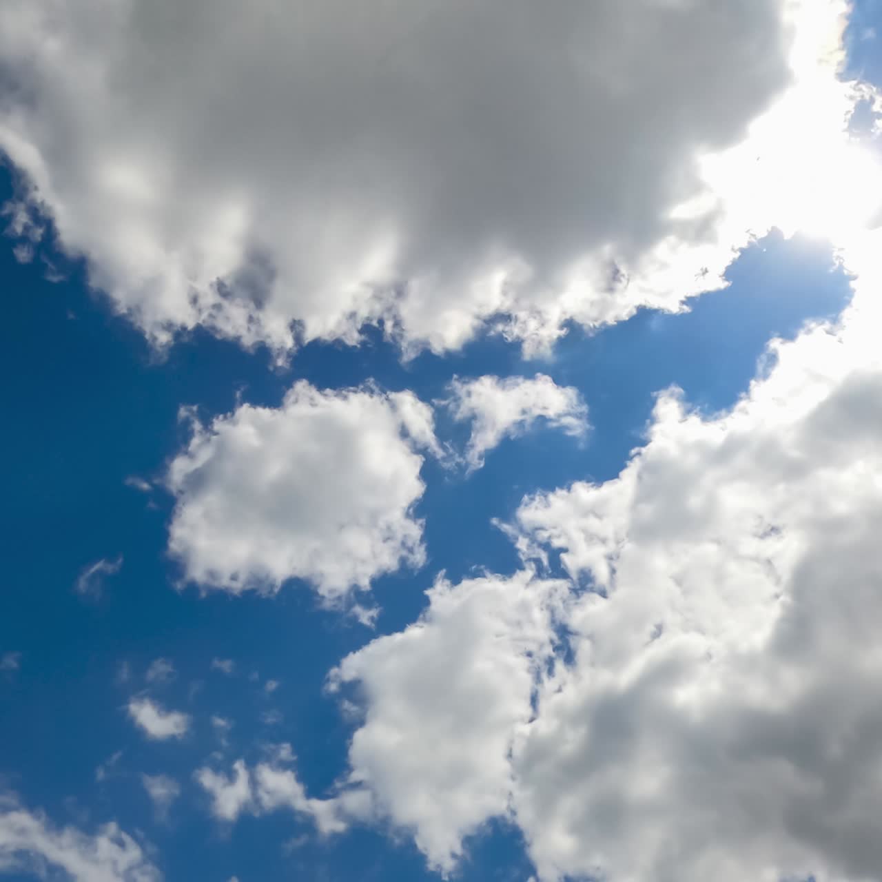 Bright sun shining in blue sky. Quickly flying white clouds against the sun. View from below. Timelapse