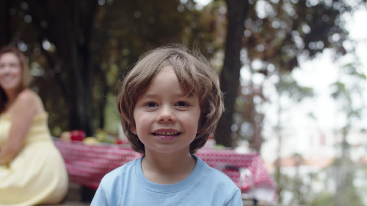 colpo medio di un ragazzino carino che posa alla macchina fotografica durante un picnic in famiglia nella foresta