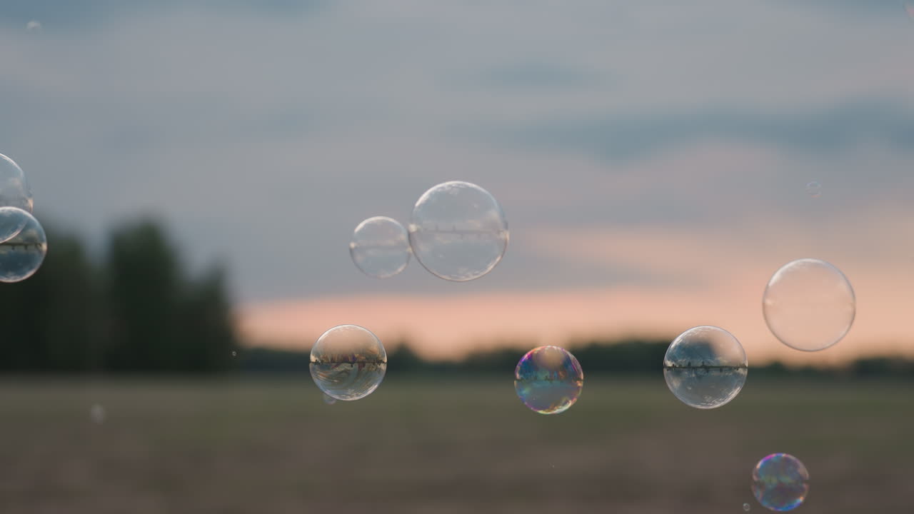 close up side view of woman blowing delicate soap bubbles over blurred country landscape at sunset lips pursed gentle breath forming iridescent spheres drifting softly across warm evening air