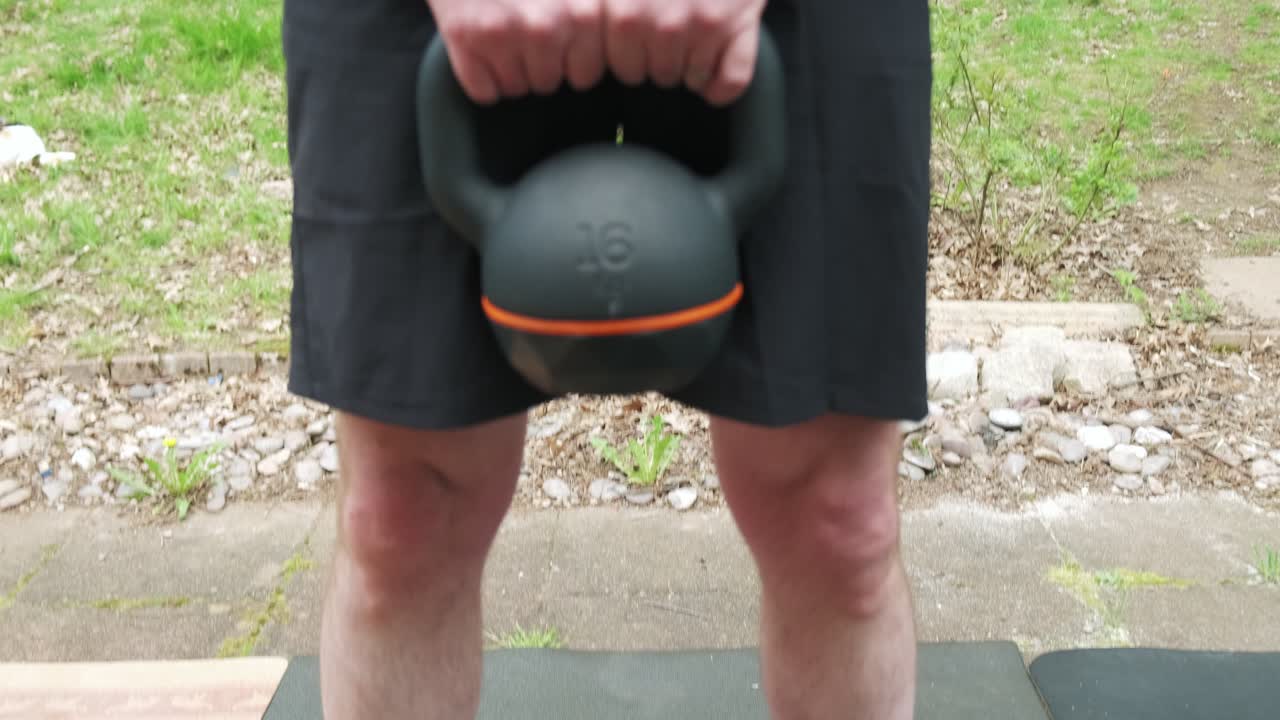 Center shot of a man doing a deadlift with a 16 kg kettlebell outside in slow motion 4K