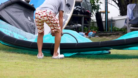 A-Man-Pumping-up-a-Wind-Surfing-Board-Sail-Resting-on-the-Ground-in-Pattaya,-Thailand