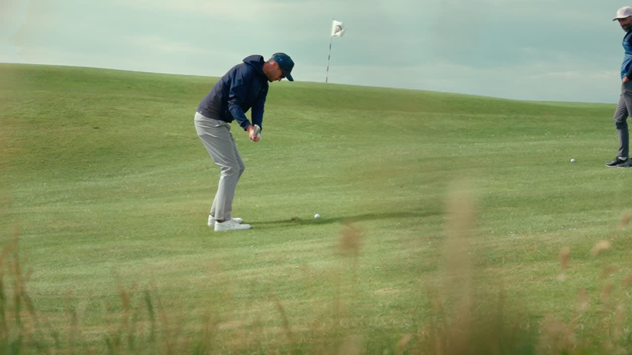 Male golfer goes up and down for par using wedge for chip shot onto green with flag stick blowing in the breeze on Ireland links golf course