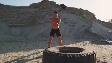 atleta muscular hombre fuerte golpea un martillo en una rueda enorme en las montañas arenosas en cámara lenta. entrenamiento de fuerza y resistencia para luchadores