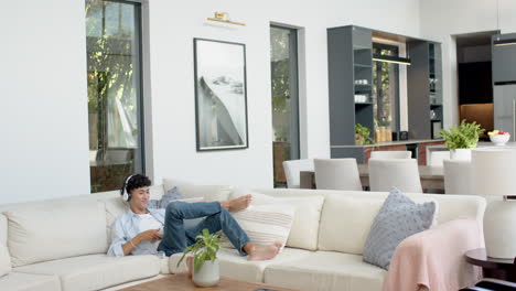 relaxing on sofa, teenage boy with headphones using tablet in modern living room
