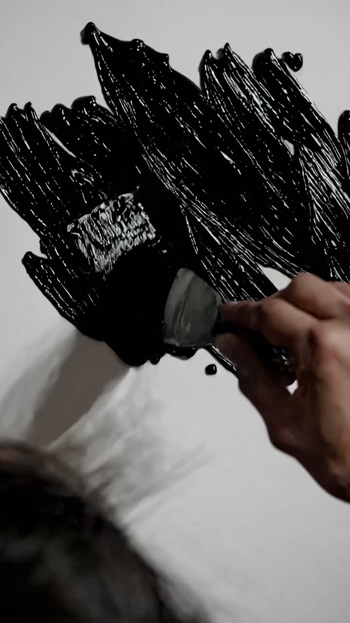 Close-up video shot from above of a hand painting a wall with black paint, showcasing the texture