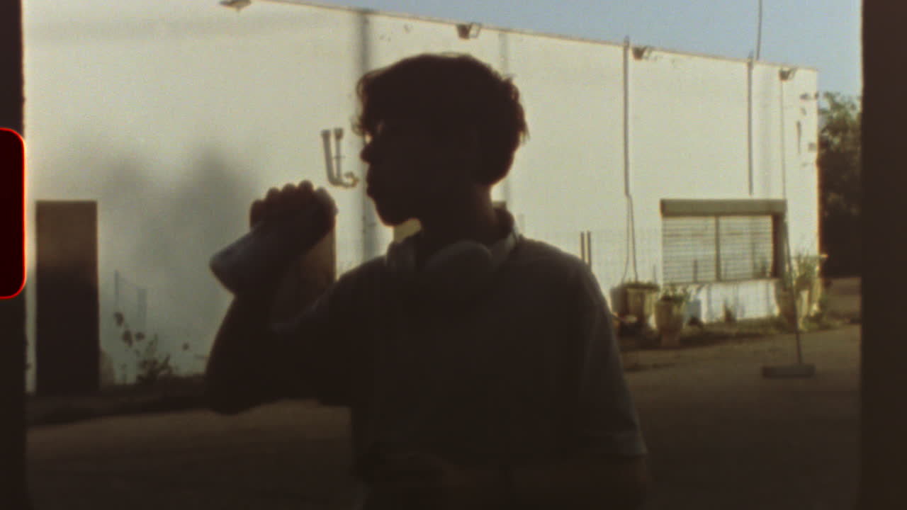 Filmed on super 8 film Vintage, retro style super 8 movie showing a teenager drinking and eating with a white industrial building in the background