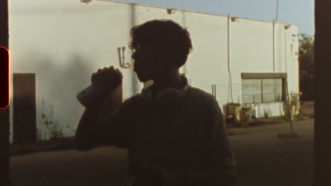 filmed on super 8 film vintage, retro style super 8 movie showing a teenager drinking and eating with a white industrial building in the background