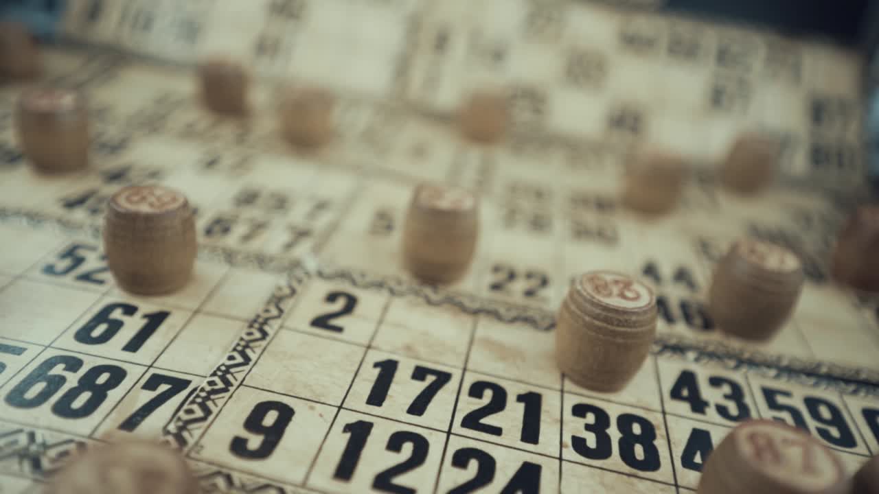 video macro de un tablero de bingo, luces de estudio, 120 fps, cámara lenta, dígitos de chips de madera, imágenes en bruto, juego de mesa de lotería vintage, números de cartas, grúa tira hacia atrás movimiento de moda